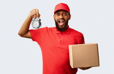 Acil teslimat servisi. Afro-Amerikan Kurye Saati, sarı arka planda duran karton kutuyu teslim ediyor. Stüdyo Çekimi