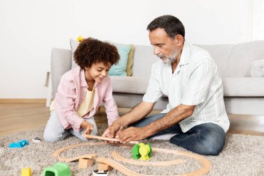 A grandfather and his young grandson share a joyful moment together, playing with toys on the floor. They are engaged and smiling, creating a warm atmosphere of love and connection. clipart