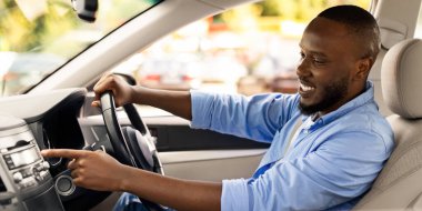 Yol Çalma Listesi. Otomobil kullanan ve otomatik ses sisteminde müzik dinleyen mutlu siyahi adam portresinin yan görünümü, test sürüşü sırasında radyoyu açarken otomobil seçeneklerini kontrol etmek