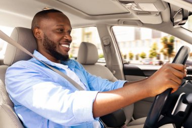 Kendine güvenen profesyonel sürücü. Sürücü koltuğunda oturan gülümseyen Afrikalı Amerikalı bir adamın yan görünüm portresi. Pozitif siyah adam şehirde direksiyonda el ele tutuşuyor.