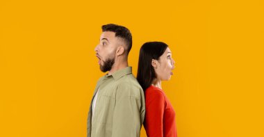 Genç bir çift, şaşkınlık ifadeleriyle sırt sırta vererek oyuncu ilişkilerini sergiliyor. Parlak sarı arka plan, beraberliğin ve aşkın neşeli atmosferine eklenir..