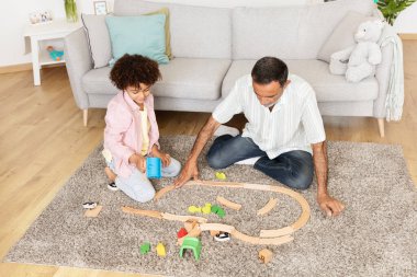 Büyükbaba torunuyla yerde oturur ve birlikte oyuncak tren rayı inşa eder. Sıcak ve sevgi dolu bir oturma odasında kaliteli zaman geçiriyorlar..