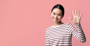 Hoş geldiniz. Dost canlısı, güzel bir Asyalı kadının el sallamasının portresi, Pembe Stüdyo 'nun arka planında tek başına dururken genç ve olumlu Koreli bir bayanın selamlaması,