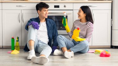 Pozitif Asyalı çift tekme attıktan sonra yerde oturuyor, ev bakımından sonra dinleniyor ve eğleniyorlar. Sevgi dolu genç adam ve kadın yeni evlerini temizlerken ara veriyorlar.