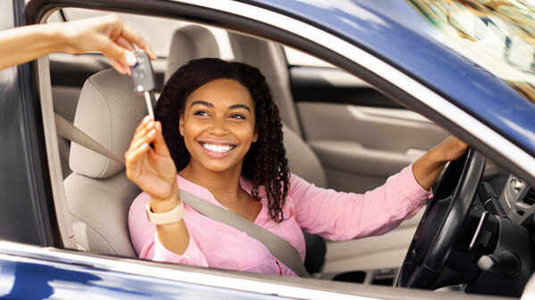 Продажа автомобилей. Менеджер дает новый ключ к счастливой молодой черной леди в магазине дилеров, избирательный фокус. Возбужденный афроамериканский покупатель покупает автомобиль у продавца в автосалоне