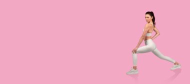 Bir kadın, güçlü ve esneklik gösteren canlı pembe bir zemin üzerinde hamle egzersizi yapıyor. Spor kıyafetleri giyiyor ve seans boyunca formda kalıyor..