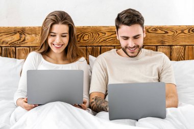 Birlikte vakit geçiririz. Genç gülümseyen karı koca yatakta oturup dizüstü bilgisayarlara, panorama, boş alana bakıyorlar.
