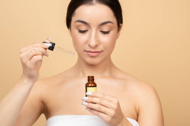 Genç beyaz bir kadın, bir damlatıcıyı kullanarak bir cilt bakım serumu uygulamaya odaklanmış. Cildini sakin ve minimalist bir ortamda büyütüyor. Kendine bakmanın tadını çıkarıyor..