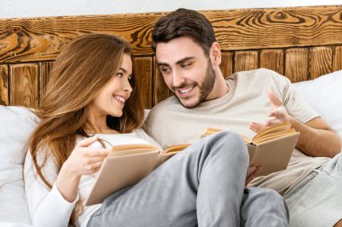 Çift akşamları yatak odasında kitap okur. Gülümseyen adam ve kız evde giyinmiş yataktalar..
