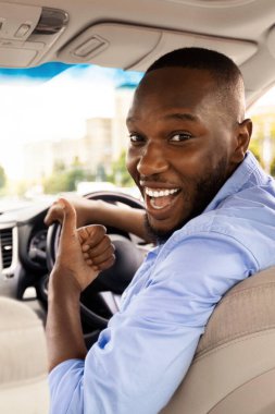 Harika araba. Mutlu Genç Siyah Adam İşaret İşaretini Gösteriyor, Yeni Otomobil Alma Mağazasında oturuyor, Tatilin tadını çıkarıyor, Yolcuya Bakıyor, Arka Koltuktan Bakıyor,