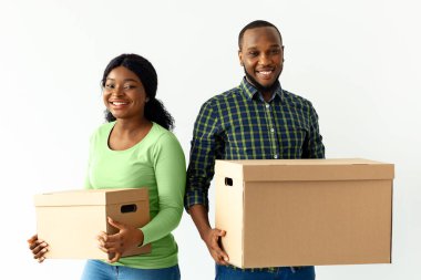 Yer değiştirme konsepti. Karton kutular taşıyan ve kameraya gülümseyen neşeli siyah milenyum eşleri, yeni dairelerine taşındıkları için mutlu Afrikalı Amerikalı çiftler.