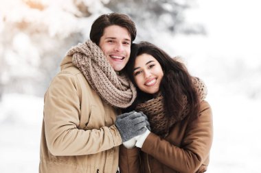 Kış buluşması konsepti. Mutlu kız arkadaş ve erkek arkadaş el ele tutuşup Noel sabahı ormanda kameraya bakıyor.