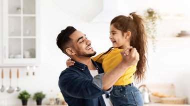 Neşeli bir Arap babanın evde kızıyla dans edişinin portresi, mutlu bir ortadoğulu baba ve tatlı bir çocuğun mutfak içinde birlikte eğlenmesi, gülmesi ve gülümsemesi, boş bir alan.