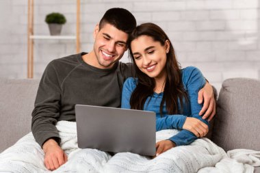 Ev Kavramında Kalın. Tek başına yaşayan eşler dizüstü bilgisayarda film izleyip sarılıyor koltukta oturuyor, boşluğu kopyalıyor.