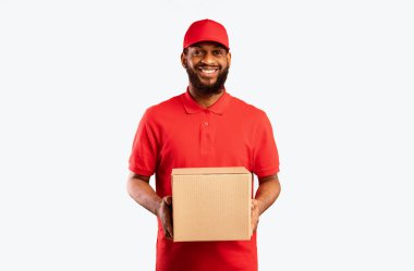 Afrikalı Amerikalı Dağıtım elemanı karton kutu tutuyor. Stüdyoda sarı arka planda bekleyen müşterilere çevrimiçi sipariş veriyor.