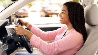 Afro-Amerikalı bir kadının araba kullanırken, galeride test sürüşü yaparken yan görünüm portresi. Yeni, güzel bir arabaya binen mutlu bir bayan lüks bir otomobilde sürücü koltuğunda oturuyor.