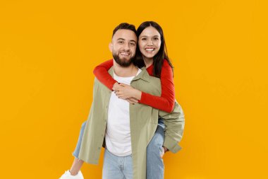 Her ikisi de neşeli görünen genç bir çift, erkeğin sırtındaki kadınla neşeli bir anı paylaşıyor. Gülümsüyorlar ve sıcaklıkla dolu canlı bir ortamda şefkat gösteriyorlar..