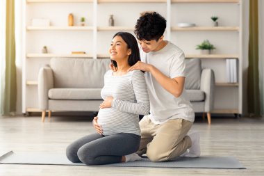 Asyalı bir adamın hamile karısının omuzlarını ovalaması, sahtesiyle panorama yapması. Çinli ailelerin hamilelik süresince sağlıklı bir yaşam sürmelerini ve evde spor yapmalarını beklemekten mutluluk duyarım.