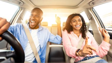 Yol Yolculuğu Konsepti. Heyecanlı Afro-Amerikan çiftin ön manzara portresi. Lüks araba sürüyorlar, müzik eşliğinde dans ediyorlar ve favori şarkılarını söylüyorlar, hafta sonları dinleniyorlar, tatile gidiyorlar, güneş parlıyor.