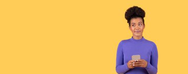 Genç bir İspanyol kadın, canlı sarı bir arkaplanda elinde akıllı telefonuyla tek başına dikiliyor. Düşünceli ve meşgul görünüyor, modern bir yaşam tarzını somutlaştırıyor, boşluğu kopyalıyor.