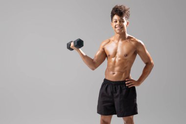 Genç Brezilyalı bir adam elinde bir dambıl tutarak spor yapmaya olan bağlılığını gösteriyor. Modern bir spor salonunda formda ve sağlıklı bir yaşam tarzını benimsiyor..