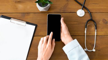 Kadın doktor, tablet ve elmalı ahşap masada boş ekranla akıllı telefondan yazı yazıyor.