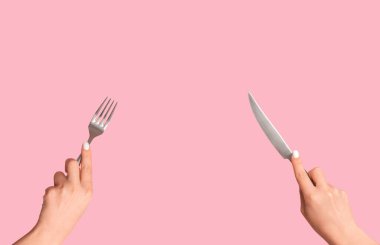 Pembe arka planda metal bıçak ve çatal tutan kız elleri, panorama