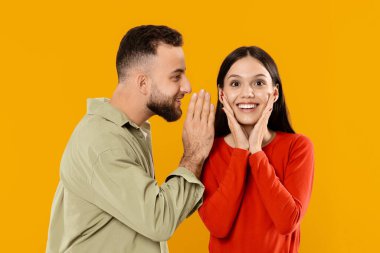 Genç bir çift, erkek kadına tatlı bir şeyler fısıldarken sevgisini ifade eder. Şaşkınlık ve sevinçle tepki verir, onların neşeli bağlarını vurgular..