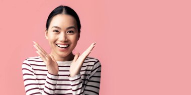 Şaşırmış Koreli genç bayan ellerini kaldırıyor ve kameraya heyecanla bakıyor Asyalı kadının iyi habere duygusal tepki göstermesi ya da iyi bir teklif sunması, pembe arka planda tek başına dikilmesi,