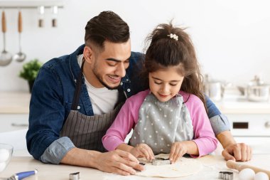 Arap baba ve küçük kızı sevmek mutfakta yemek yaparken eğlenmek, tatlı küçük kız hamurdan farklı kurabiye şekilleri kesiyor, babayla evde yemek pişirmekten hoşlanıyor, boş alan.