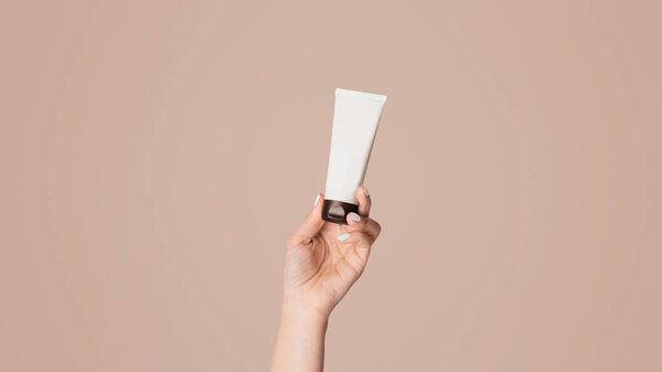 Unrecognizable woman showing tube with hand cream over pink background, closeup. Panorama
