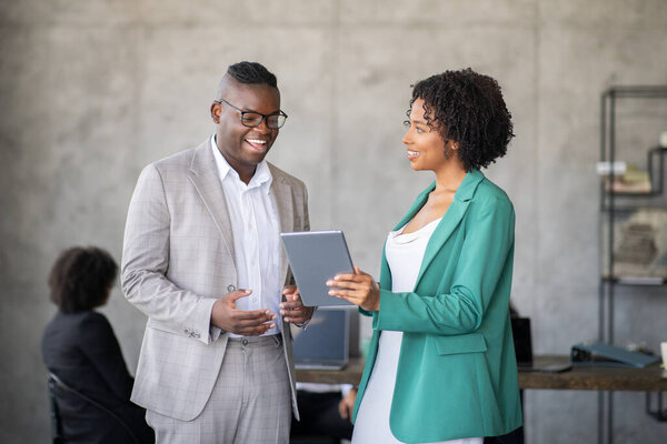 Два профессионала участвуют в дискуссии, рассматривая цифровой планшет в современном офисе. Они демонстрируют командную работу и сотрудничество в различных бизнес-условиях.