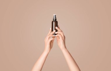 Elinde krema, yağ, losyon ya da pembe arka planda serum olan bir şişe tutan genç kız, yakın plan. Panorama