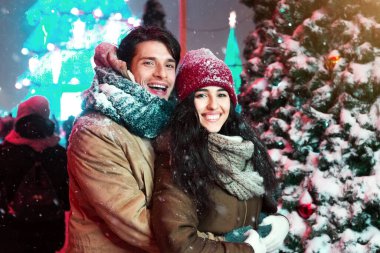 Mutlu çift, süslenmiş Noel ağacının yanında sarılıyor ve gece şehir dışında buluşuyorlar. Boşluğu Kopyala