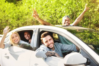 Cheerful young diverse friends riding their car, looking through windows, waving and gesturing, going on road trip together. Millennial multinational students having summertime adventure clipart