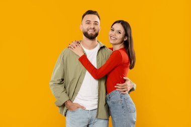 Genç bir çift sıcak bir kucaklaşmayla birbirine yakın durur, mutluluk ve sevgiyi ifade ederler. Parlak gülüşleri ve neşeli tavırları şefkatlerini neşeli ve izole bir ortamda vurguluyor..