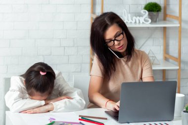 Laptop 'ta çalışan ve evde telefonla konuşan meşgul bir anne, yakınlarda oturan depresif bir çocuk. Covid-19 karantinası sırasında internetteki işi yüzünden çocuğa ayıracak vakti olmayan genç anne.