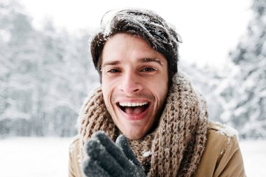 Kışın tadını çıkar. Mutlu Adam Elleri ovuşturuyor Kameraya gülümsüyor Karlı Ormanda duruyor