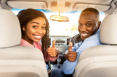 Test sürüşü, harika sürüş, iyi araba konsepti. Heyecanlı Afrikalı Amerikalı Çiftin Portresi İşaret İşaretini Gösteriyor, Yeni Otomotiv 'de ön koltuklarda oturuyor, Dükkandaki Kamera Alma Aracına Bakıyor