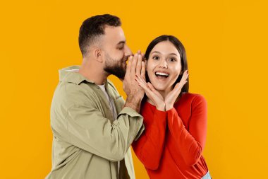 Genç bir çift, kadının kulağına fısıldayan adamla sevgi dolu bir anı paylaşıyor. Gülüyorlar ve birbirlerine eşlik ederek eğleniyorlar. Parlak sarı bir arka plana karşı..