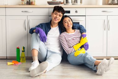 Çalışkan Asyalı çift birlikte evi temizlerken mola veriyor, fırının yanında oturan genç adam ve kadın gülümsüyor, sarılıyor, temizlik malzemesi yiyor, mutfak içini temizliyor, fotokopi çekiyor.