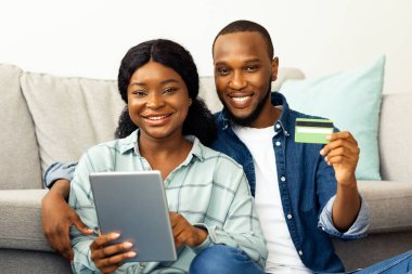 Çevrimiçi alışverişler. Dijital tabletli ve kredi kartlı mutlu siyah çift internetten alışveriş yapıyor, Afrikalı eşler yeni daireye taşındıktan sonra mobilya veya ev dekorasyonu sipariş ediyor,
