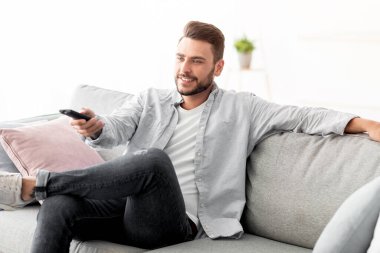 Boş zaman ve eğlence. Mutlu adam televizyon izliyor uzaktan kumandayla televizyon kanallarını değiştiriyor evdeki kanepede oturuyor, uzayı kopyalıyor. TV programlama kavramı