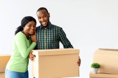 Neşeli genç Afrikalı Amerikalı eşler taşınma gününde karton kutularla poz veriyorlar, mutlu siyah çift yeni evlerine taşınırken, kameraya sarılıp gülümserken,