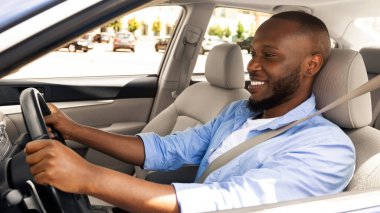 Yeni araba kullanan mutlu Afrikalı Amerikalı genç adam, ofise ya da tatile gidiyor, dışarıdan çekilmiş, profil manzaralı. Yakışıklı, başarılı adam, iyi bir günün ardından eve dönüyor, yola bakıyor ve gülümsüyor.