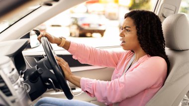 Kızgın siyah kadın araba sürücüsü birine bağırıyor, kazaya duygusal tepki veriyor ya da yüz ifadesi bozuk, direksiyona basıyor kornaya basıyor, profil görüş açısına bakıyor.