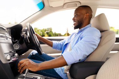 Modern araçta oturan, direksiyon ve vites kolu tutan deneyimli erkek sürücünün yeni el arabasına odaklanmış genç Afrikalı Amerikalı adamın profiline bakın.