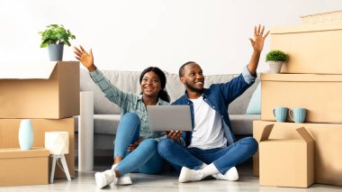 Yeni evlerinde dizüstü bilgisayarlarıyla oturan mutlu siyah çift, iç dizayn etmeyi hayal ediyorlar, bilgisayar tasarımlı genç Afrikalı Amerikalı eşler, kendi dairesine taşındıktan sonra daire dekorasyonu yapıyorlar,