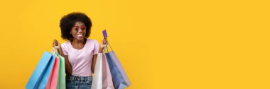 Mutlu müşteri. Alışveriş torbaları ve limitsiz kredi kartıyla gülümseyen neşeli siyahi kadın. Sarı arka planda gülümseyen kadın, alışveriş manyakları, fotokopi alanı.