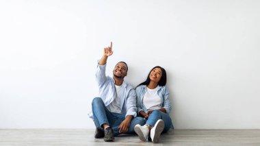 İç mekan, dekorasyon ve mobilya planlayan Afrikalı Amerikalı bir çift yerde oturuyor ve boş bir yeri işaret ediyor.